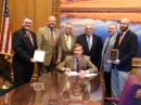 At the bill signing (L-R): Colorado Sen Chris Holbert; SEC and SGL Robert Wareham, N0ESQ; SM Jack Ciaccia, WM0G; Gov John Hickenlooper; Rocky Mountain Division Vice Director Jeff Ryan, K0RM; ASEC Perry Lundquist, W6AUN, and Rep Jonathan Singer. Holbert and Singer are holding their ARRL Special Services Award plaques. [John Maxwell, W0VG, photo]